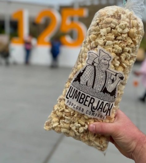 A bag of Lumberjack kettle corn held up in front of the 125 sign at the Washington State Fair