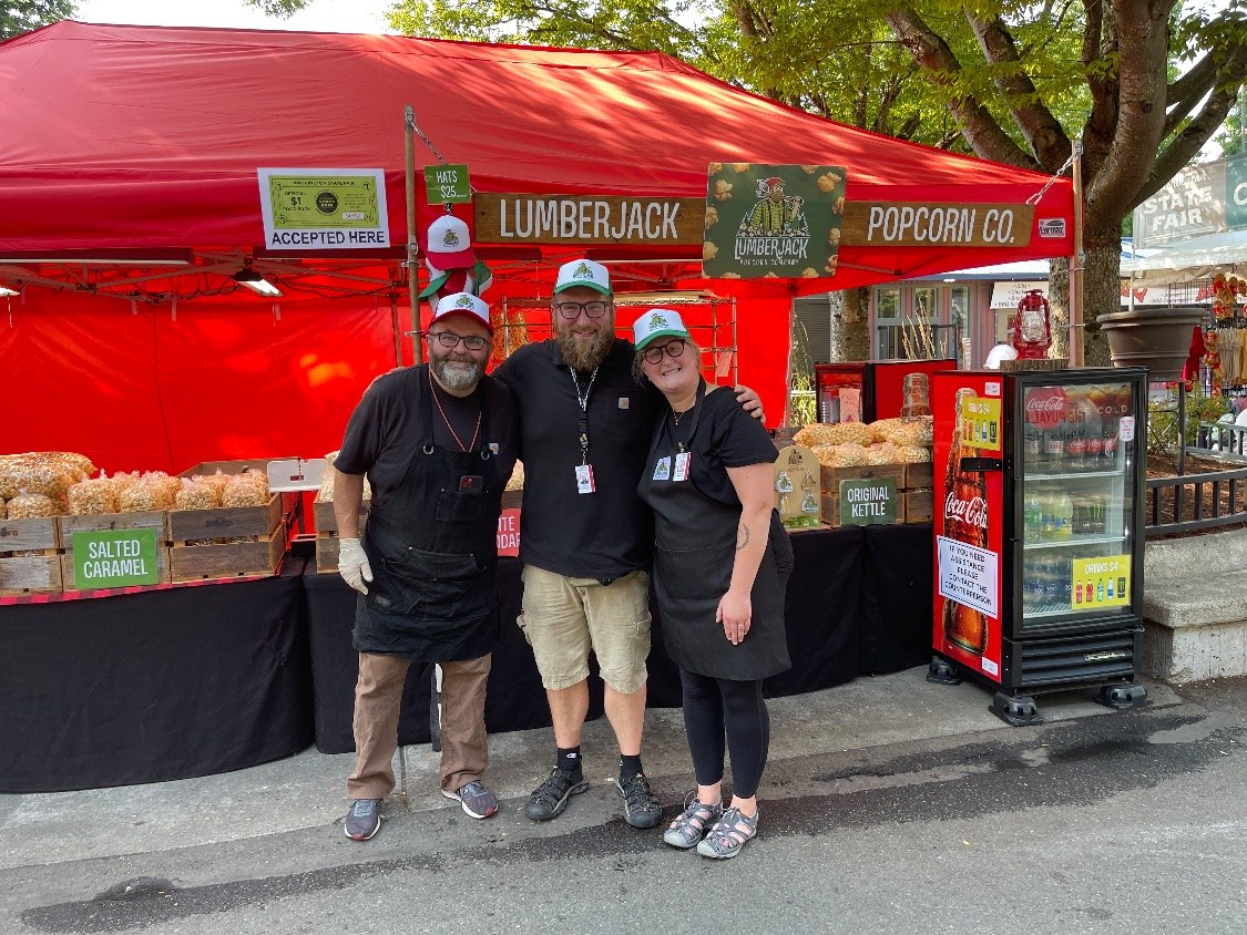 Greg, Nate, and Taylor in matching Lumberjack hats in front of the Lumberjack Popcorn Co. booth at the Washington State Fair