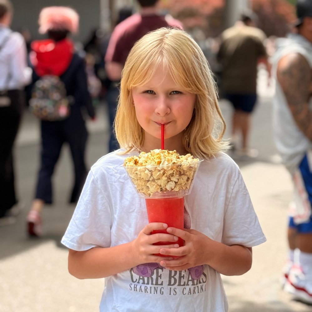 A young fairgoer sipping lemonade from a cup topped with a bowl of Lumberjack popcorn