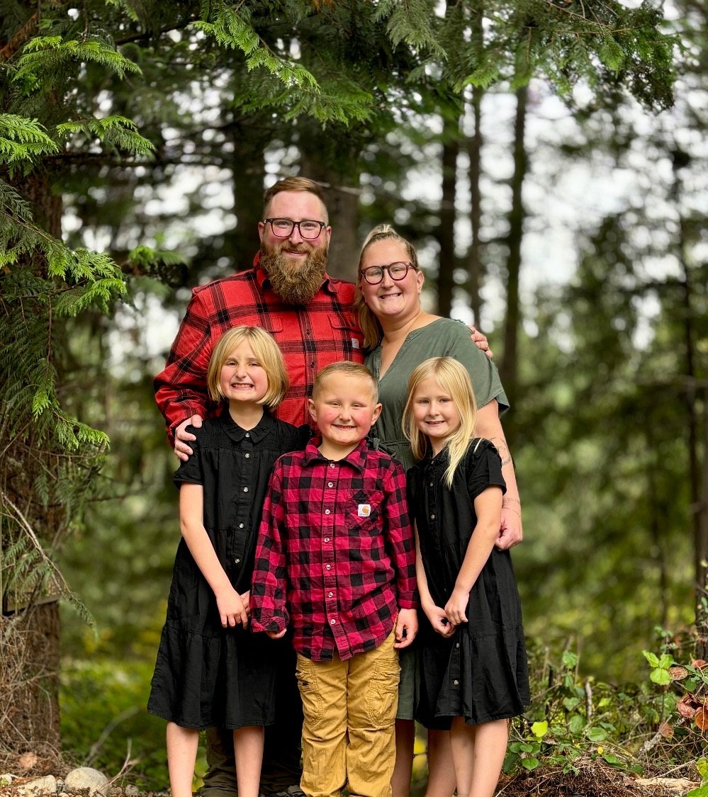 Nate, Taylor, and their three kids in matching red plaid and black outfits in the forest