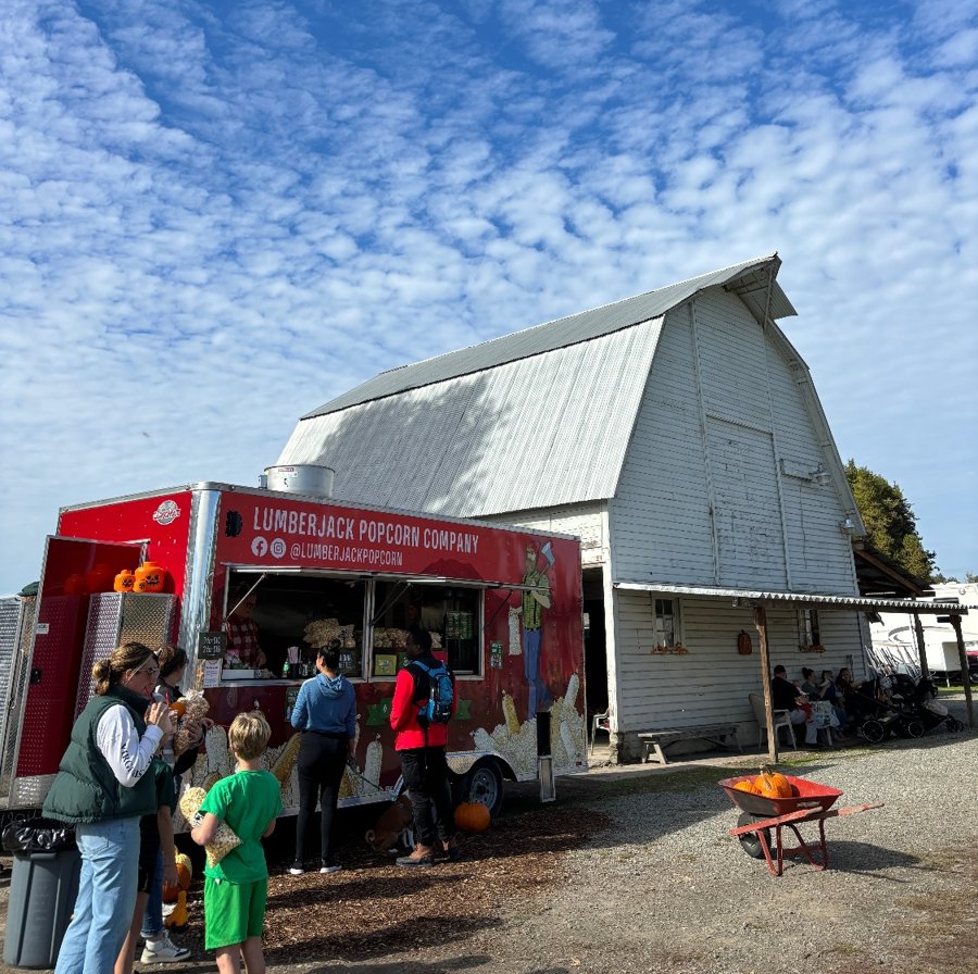 Customers lined up at the red Lumberjack Popcorn Company trailer next to a white barn
